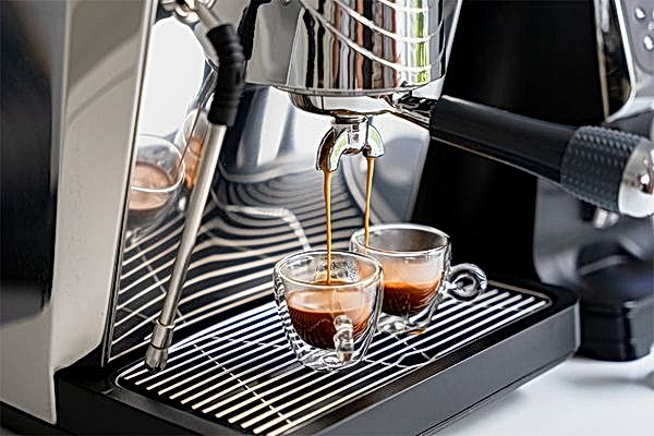 2 Espressotassen stehen in einer Kaffeemaschine und werden von ihr befüllt