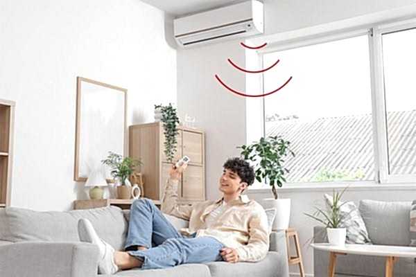 Junger Erwachsener liegt fröhlich auf Sofa und bedient eine Klimaanlage per Fernbedienung