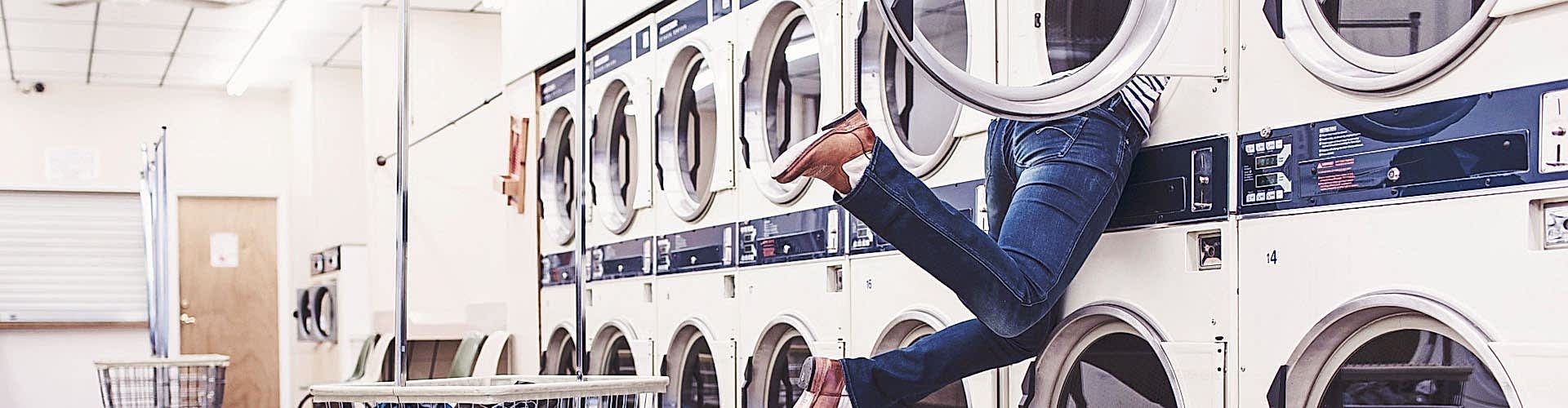 Eine Person steckt mit dem Oberkörper in einer Waschmaschine eines Waschsalons fest