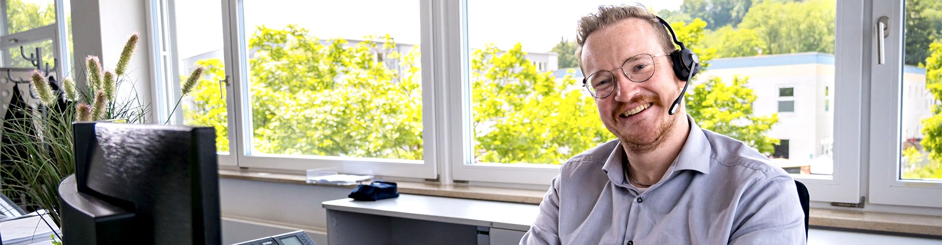 Mitarbeiter sitzt vor seinem Monitor am Schreibtisch und lächelt