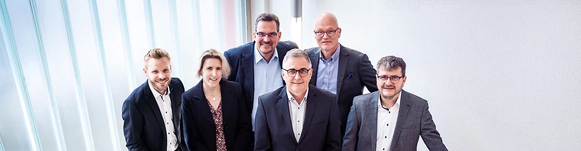 5 Personen in Sakko stehen auf einer Treppe